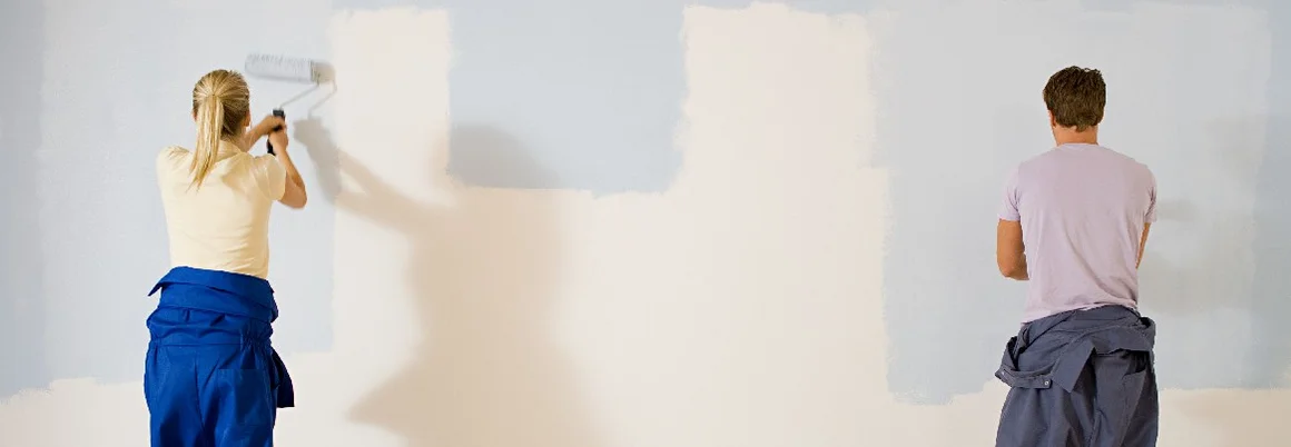 Zwei Personen streichen Wand mit Farbrolle